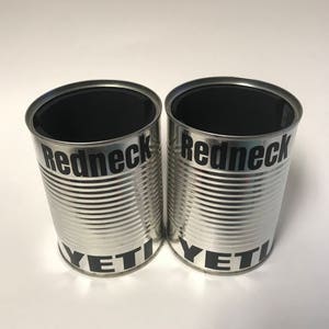 Peut inclure: Deux récipients cylindriques argentés avec des intérieurs noirs. Le mot "Redneck" est imprimé en noir sur la partie supérieure de chaque récipient, et "YETI" est imprimé en noir sur la partie inférieure. Les récipients sont sur une surface blanche.