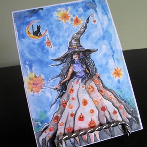 May include: Watercolor painting of a witch with long black hair wearing a pointed hat and a dress with a pumpkin pattern. She is holding a wand with a spark at the end. The background is a blue sky with stars and a crescent moon.