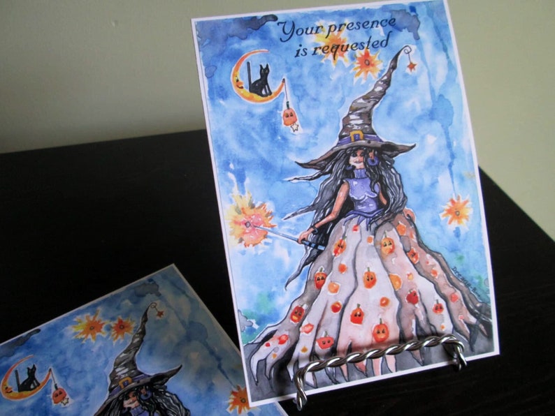 May include: A watercolor painting of a witch with a black cat on a crescent moon. The witch is wearing a purple dress and a hat with a wide brim. The background is a blue sky with stars and pumpkins. The text "Your presence is requested" is written at the top of the card.