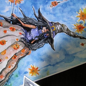 May include: A watercolor painting of a witch flying through the air with a wand in her hand. She is wearing a purple dress and a brown hat with a buckle. The background is a blue sky with clouds and stars.