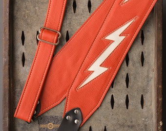 Correa de guitarra de cuero con incrustaciones de cuero de 3" con diseño de rayo en color naranja y blanco
