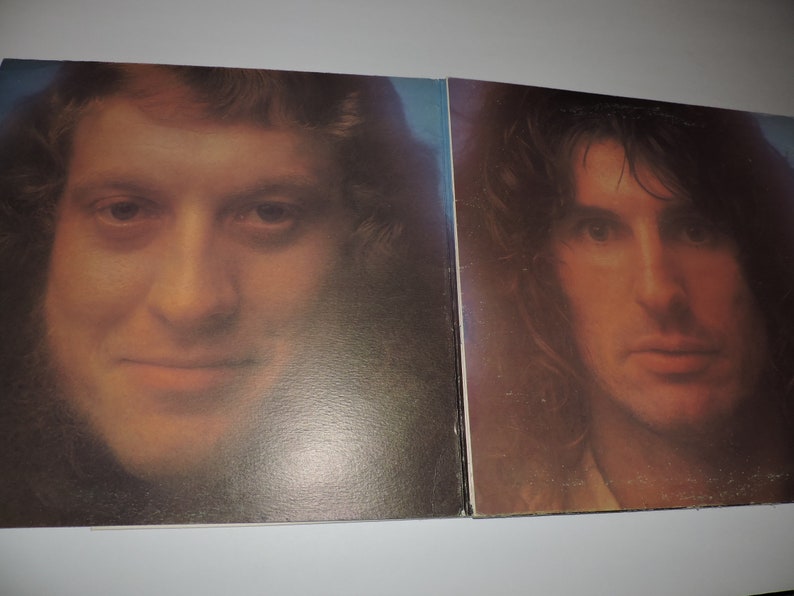May include: Close-up of a vintage vinyl record album cover featuring two men with long hair. The men are looking directly at the camera. The album cover is a warm brown color.