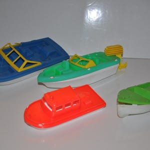 May include: Four plastic toy boats in different colours and styles. A blue and white boat, a green and white boat, a red and white boat, and a green boat.