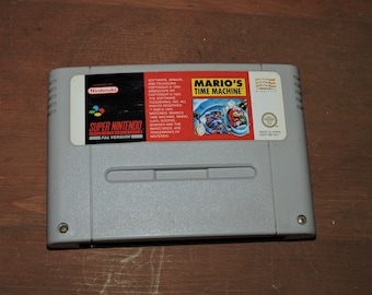 May include: A Super Nintendo Entertainment System game cartridge for Mario's Time Machine. The cartridge is gray with a red and white label featuring Mario and Luigi.