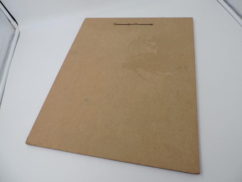 Op de afbeelding: Een rechthoekige, bruine kartonnen achterplaat met een klein gaatje aan de bovenkant om op te hangen. De plaat heeft een licht getextureerd oppervlak en is in de afbeelding schuin geplaatst. De achtergrond is wit.