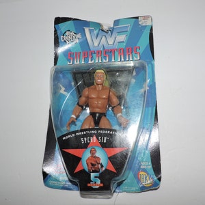 May include: A WWF Superstar action figure of Sycho Sid in a blue and black wrestling ring. The figure is packaged in a clear plastic blister pack with a blue and white cardboard backing. The packaging features the WWF logo and the text "Superstars".