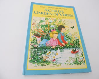 Può includere: Libro A Child's Garden of Verses di Robert Louis Stevenson. La copertina presenta un'illustrazione colorata di due bambini vicino a uno stagno con una barca a vela, circondati da fiori e vegetazione. Il libro ha un bordo blu.