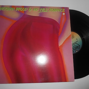 Op de afbeelding: Een vinyl platenhoes met een abstract ontwerp in roze en oranje met de tekst "Herman Brood & His Wild Romance".