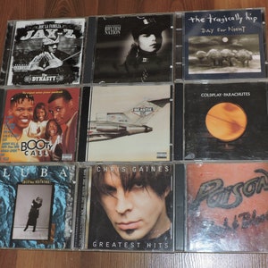 May include: A collection of nine music CDs in jewel cases. Album titles include "Dynasty" by Jay-Z, "Rhythm Nation," "Day for Night" by The Tragically Hip, "Booty Call," "Beastie," "Parachutes" by Coldplay, "Bit for Nothing" by Luba, "Greatest Hits" by Chris Gaines, and "Poison Flesh & Blood."