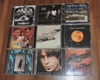 May include: A collection of nine music CDs in jewel cases. Album titles include "Dynasty" by Jay-Z, "Rhythm Nation," "Day for Night" by The Tragically Hip, "Booty Call," "Beastie," "Parachutes" by Coldplay, "Bit for Nothing" by Luba, "Greatest Hits" by Chris Gaines, and "Poison Flesh & Blood."