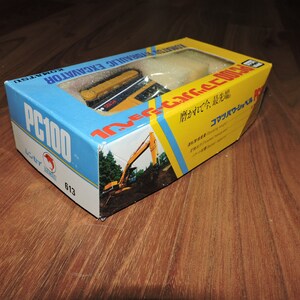 May include: A yellow and black toy excavator in a box with Japanese text. The box is labeled "Komatsu Hydraulic Excavator PC100".