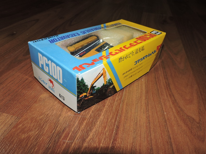 May include: A yellow and black toy excavator in a box with Japanese text. The box is labeled "Komatsu Hydraulic Excavator PC100".