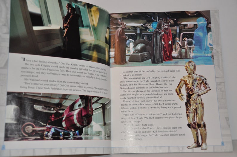 May include: A close-up image of a book open to a page with text and images from the Star Wars movie. The text describes a scene from the movie where Jedi Knights are negotiating with the Trade Federation. The image shows a scene from the movie with a Jedi Knight and a Trade Federation leader. The image also shows a close-up of C-3PO, a golden protocol droid.