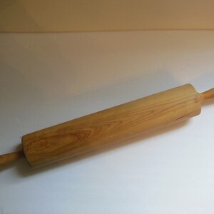 May include: A wooden rolling pin with two handles. The rolling pin is made of light brown wood with a natural grain pattern.