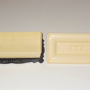 May include: A rectangular cream-colored box with a black ornate base and a matching lid. The lid has two small round buttons.