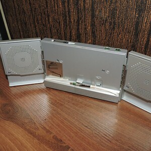 May include: A silver-colored portable speaker system with three sections. The center section has a screen and ports. The two side sections have speakers with a grill pattern.