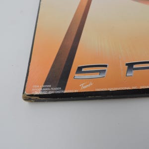 Op de afbeelding: Een rechthoekige Spider-Man-poster met een oranje en bruine achtergrond. De poster toont de letters "SP" in zilver. De tekst "ITEM # SI2559 SPIDER-MAN-TEASER PUBLISHED AND DISTRIBUTED BY Trends" staat onderaan afgedrukt.