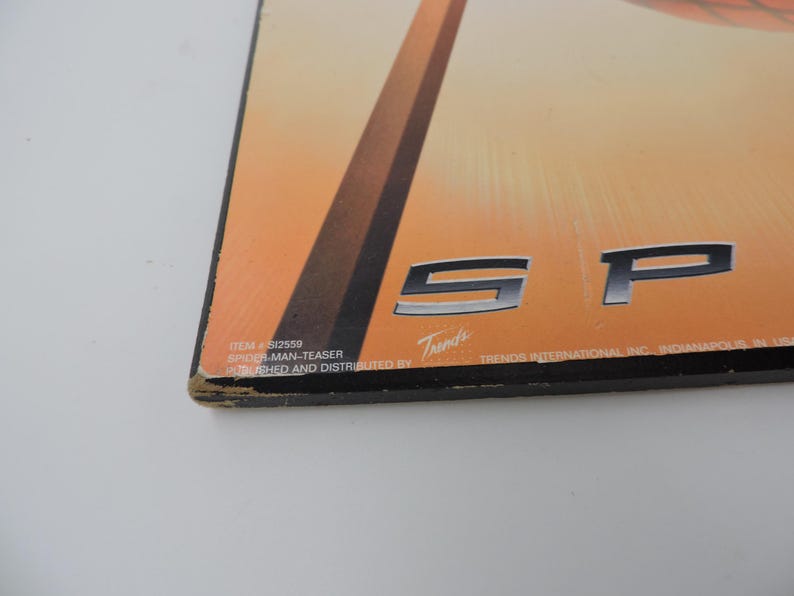 Op de afbeelding: Een rechthoekige Spider-Man-poster met een oranje en bruine achtergrond. De poster toont de letters "SP" in zilver. De tekst "ITEM # SI2559 SPIDER-MAN-TEASER PUBLISHED AND DISTRIBUTED BY Trends" staat onderaan afgedrukt.