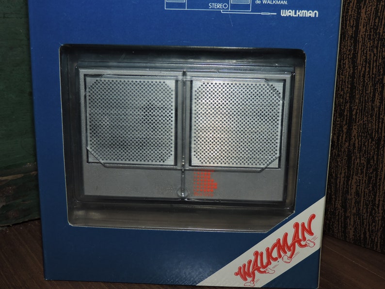 May include: A silver and black cassette player with a Walkman logo on the front. The player is in a blue and white box with the word "Walkman" printed on the side.