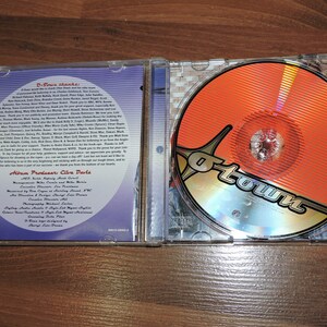 May include: A CD case with a blue and silver background. The front cover features a red and gold disc with the word "O-Town" in a stylised font. The back cover features a list of credits and thanks.