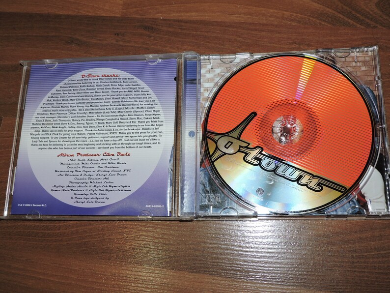 May include: A CD case with a blue and silver background. The front cover features a red and gold disc with the word "O-Town" in a stylised font. The back cover features a list of credits and thanks.