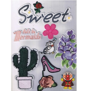 May include: A collection of iron-on patches featuring a variety of designs, including a cactus, a flower, a cat, a high heel, a rose, a cartoon character, and text that says "Let's be mermaids" and "Sweet".