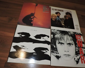 Puede incluir: Cuatro portadas de álbumes de U2: "Under a Blood Red Sky", "October", "Boy" y "War". La portada de "Under a Blood Red Sky" tiene una silueta. "October" presenta a la banda. "Boy" tiene arte en blanco y negro. "War" tiene la cara de un niño.