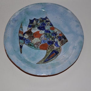 Peut inclure: Une assiette en céramique bleue avec un motif de poisson coloré. Le poisson est composé de formes géométriques et de motifs dans des tons de bleu, vert, rouge et blanc.