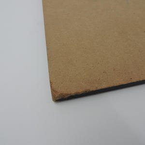 Op de afbeelding: Een hoekweergave van een rechthoekig, bruin, onafgewerkt houten bord. Het bord heeft een donkere rand en een ruw, getextureerd oppervlak. De hoek toont een licht beschadigde rand.