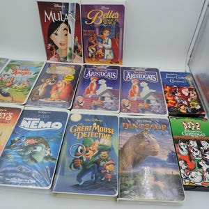 Pu&ograve; includere: Una collezione di VHS Disney con film d'animazione come "Mulan", "Alla ricerca di Nemo", "Gli Aristogatti" e "La carica dei 101 - Natale". Le cassette hanno copertine colorate con illustrazioni dei personaggi.