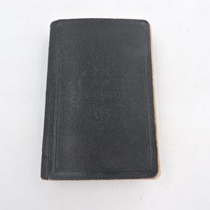May include: A small, rectangular, black book with a textured cover. The edges of the pages are visible, and the book appears to be closed. The cover has a subtle embossed design. The book is set against a white background.