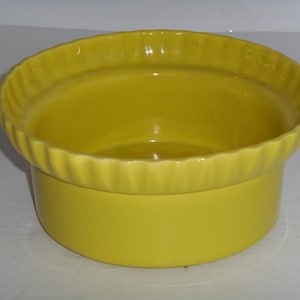 May include: A bright yellow ceramic planter with a fluted rim. The planter is round and has a smooth, glossy finish.