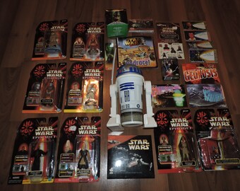 May include: A collection of Star Wars toys and merchandise, including action figures, trading cards, a book, and an R2-D2-shaped drinking cup. The toys are from the Star Wars Episode I: Phantom Menace film.