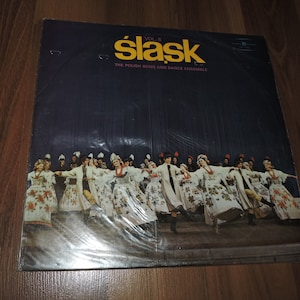 May include: A black vinyl record album cover featuring a group of people in traditional Polish folk costumes dancing on stage. The album is titled "Śląsk" Vol. 8, "The Polish Song and Dance Ensemble".