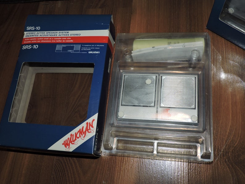 May include: A blue box with the text "SRS-10 STEREO ACTIVE SPEAKER SYSTEM ENCEINTES ACOUSTIQUES ACTIVES STEREO" and "SRS-10 WALKMAN" on it. The box is open and shows a clear plastic case with two silver speakers inside.