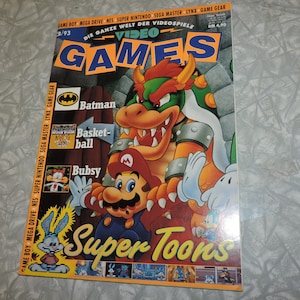 Puede incluir: Una portada de revista para Video Games, número 3/93, con una ilustración de dibujos animados de Mario, Bowser y un conejo azul. El texto de la portada dice "Video Games" y "Super Toons".