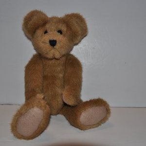 May include: A brown teddy bear with black eyes and a black nose. The bear is sitting with its legs crossed and its paws resting on its lap.