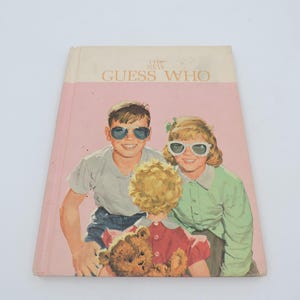 Puede incluir: Libro infantil vintage titulado "The New Guess Who" con una portada rosa y blanca. La ilustración de la portada presenta a tres niños con gafas de sol, con un osito de peluche en primer plano.