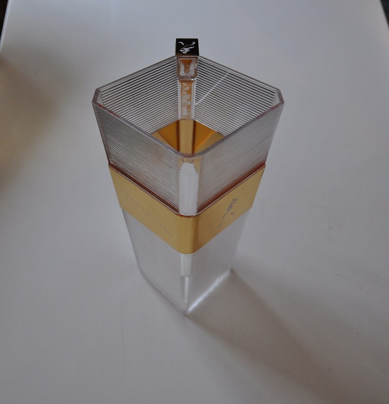 May include: A clear glass bottle with a gold band and a silver top. The bottle is empty and has a textured surface.