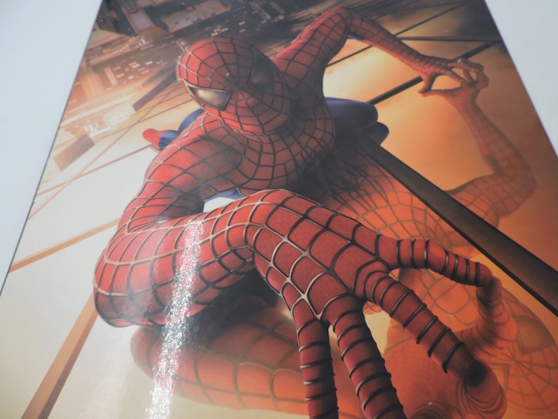 Op de afbeelding: Een dynamisch beeld van Spider-Man in zijn iconische rood-blauwe pak met webdetails. Het kunstwerk toont de behendigheid van de superheld, met een stadsachtergrond en een weerspiegeling.
