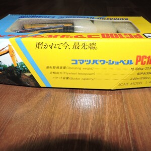 May include: A yellow toy Komatsu PC100 hydraulic excavator with a black cab and black tracks. The box is yellow and has Japanese text that reads "Komatsu Power Shovel PC100" and "Scale Model 1/48".