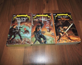 May include: Three paperback fantasy novels with illustrated covers. The books are titled "Dance of Demons", "Sea of Death", and "City of Hawks". Each book features a male character with a sword and a fantasy setting.
