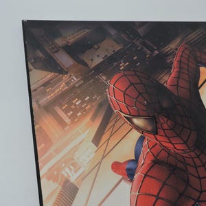 Op de afbeelding: Een ingelijste print met Spider-Man in zijn iconische rood-blauwe pak, tegen een achtergrond van een stadsgezicht. De afbeelding toont de superheld in actie, met de nadruk op zijn gedetailleerde kostuum en de stedelijke omgeving.