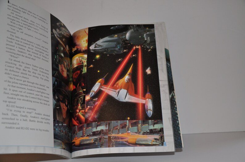 May include: A close-up of a book page with a picture of a spaceship in space. The spaceship is orange and white and has red laser beams coming from it. The text on the page reads "Anakin was streaking across the deck in his N-1 starfighter."