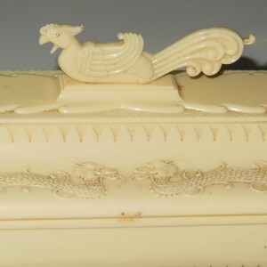 May include: A white ceramic box with a dragon design and a bird finial on the lid.