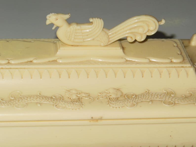 May include: A white ceramic box with a dragon design and a bird finial on the lid.