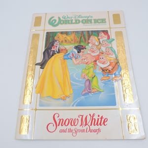 Könnte beinhalten: Vintage Buchcover für "Schneewittchen und die sieben Zwerge" aus "Walt Disney's World on Ice". Das Cover zeigt Illustrationen von Schneewittchen, der bösen Königin und den sieben Zwergen, mit goldenen Akzenten und Text.