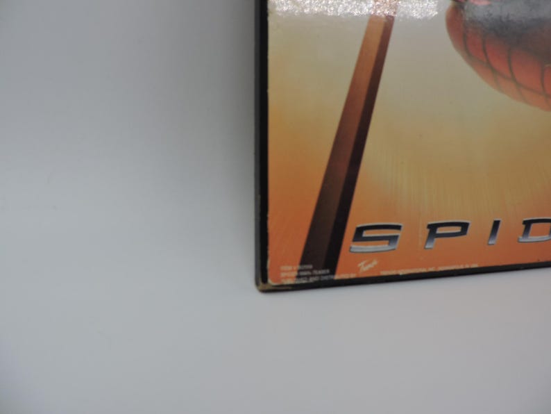 Op de afbeelding: Close-up van een doos met het woord "SPID" in zilveren letters. De achtergrond heeft een verloop van oranje en geel. De doos heeft een zwarte rand en staat op een wit oppervlak.