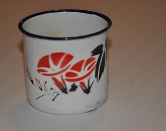 May include: White enamel mug with a black rim and a red and black floral design.