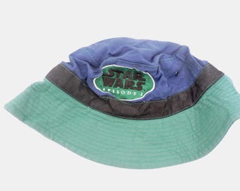 Peut inclure: Un chapeau de pêcheur bleu et vert avec le logo Star Wars Episode I. Le chapeau a une couronne bleue, un bord vert et une bande noire. Le logo Star Wars est en vert et blanc.